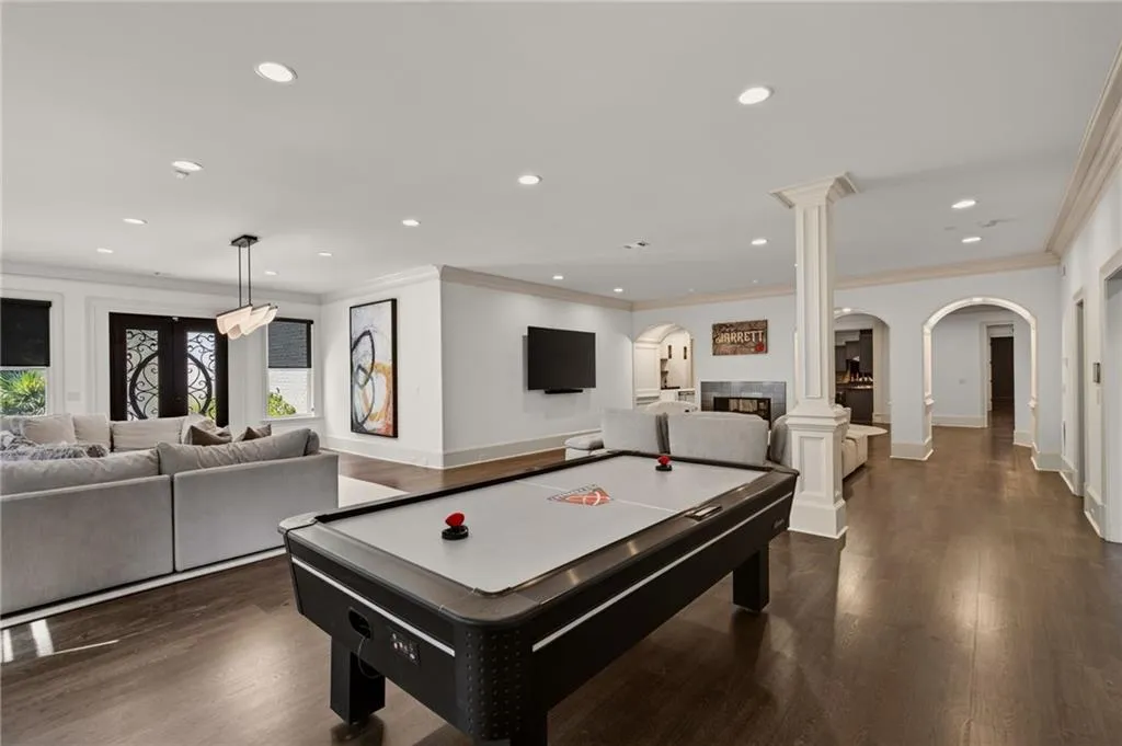 Spacious recreation area featuring dark wood-finish flooring, recessed lighting, decorative column, and multiple arched doorways