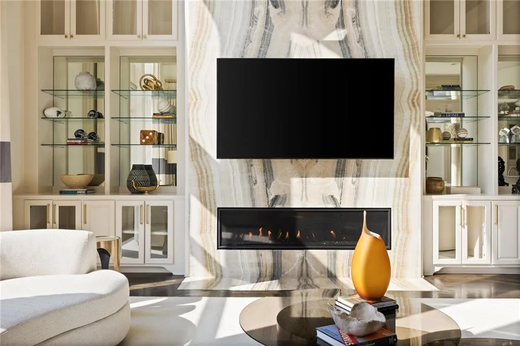 Built-in cabinetry with glass doors, integrated linear fireplace, stone-clad feature wall, and glass shelving