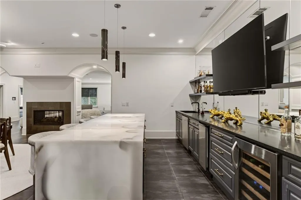 Expansive bar area featuring a large, illuminated island with a light-toned counter surface, built-in cabinetry, stainless steel appliances, and a beverage cooler