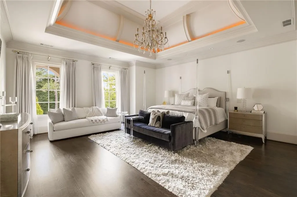 Tray ceiling with integrated lighting, wood-finish flooring, two large windows, recessed lighting, and a crystal chandelier