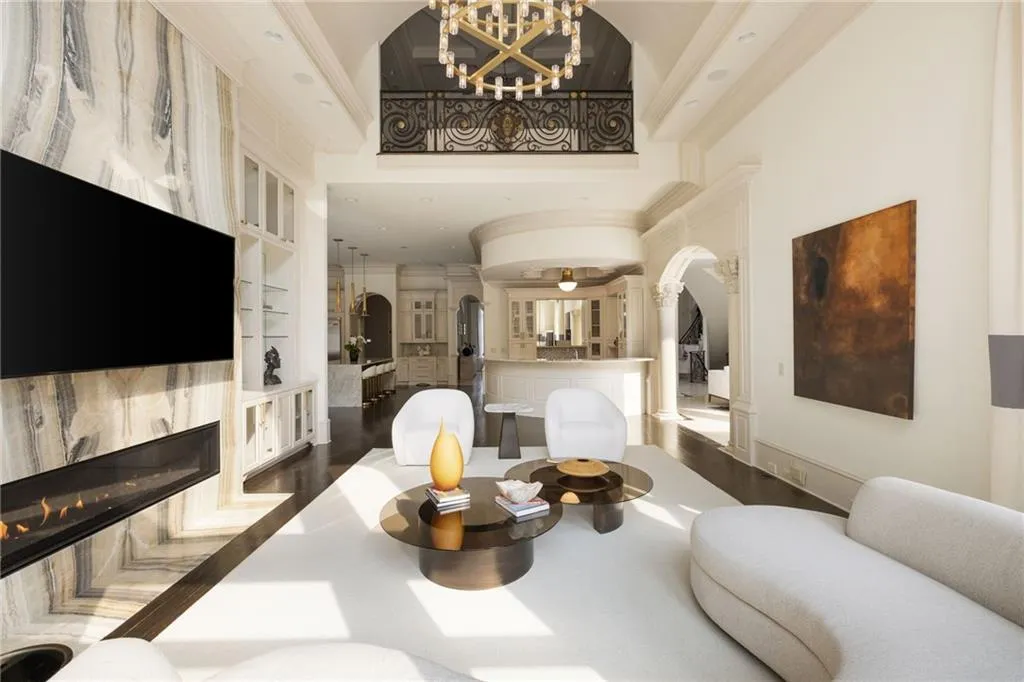 Sophisticated living room featuring floor-to-ceiling windows with natural light, a linear gas fireplace with stone surround, wall-mounted flat-screen television, built-in shelving with glass-front cabinetry, and a brass-finished chandelier with geometric detailing