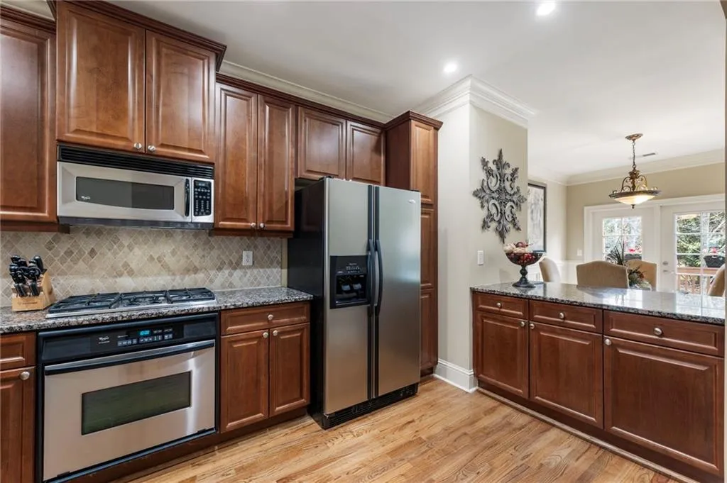 Kitchen with stainless steel appliances, dark stone counters, crown molding, light wood-style flooring, and decorative light fixtures