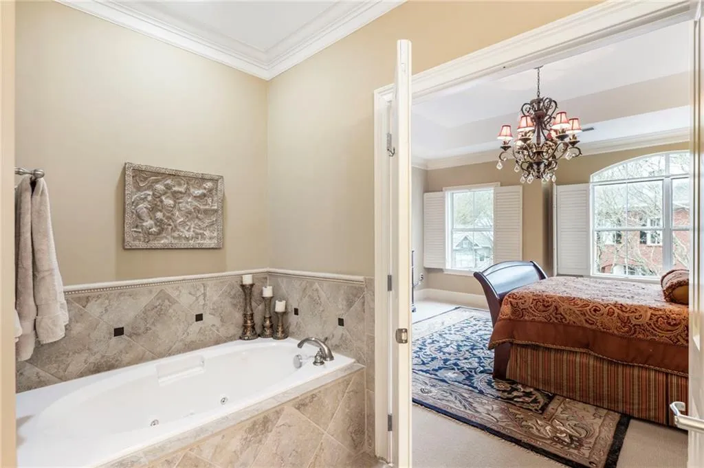 Ensuite bathroom featuring ornamental molding, a tub with jets, suspended lighting, and carpet