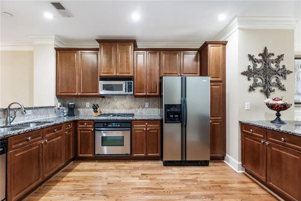 Kitchen with crown molding, stainless steel appliances, dark stone counters, light wood-style flooring, and backsplash