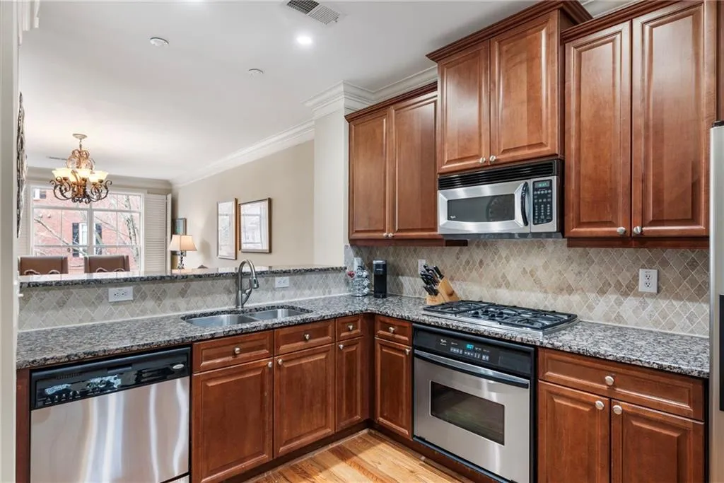 Kitchen with dark stone countertops, stainless steel appliances, crown molding, suspended lighting, and tasteful backsplash