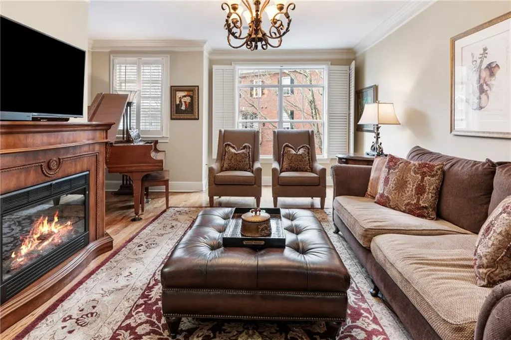 Living room with wood finished floors, a glass covered fireplace, crown molding, and suspended lighting