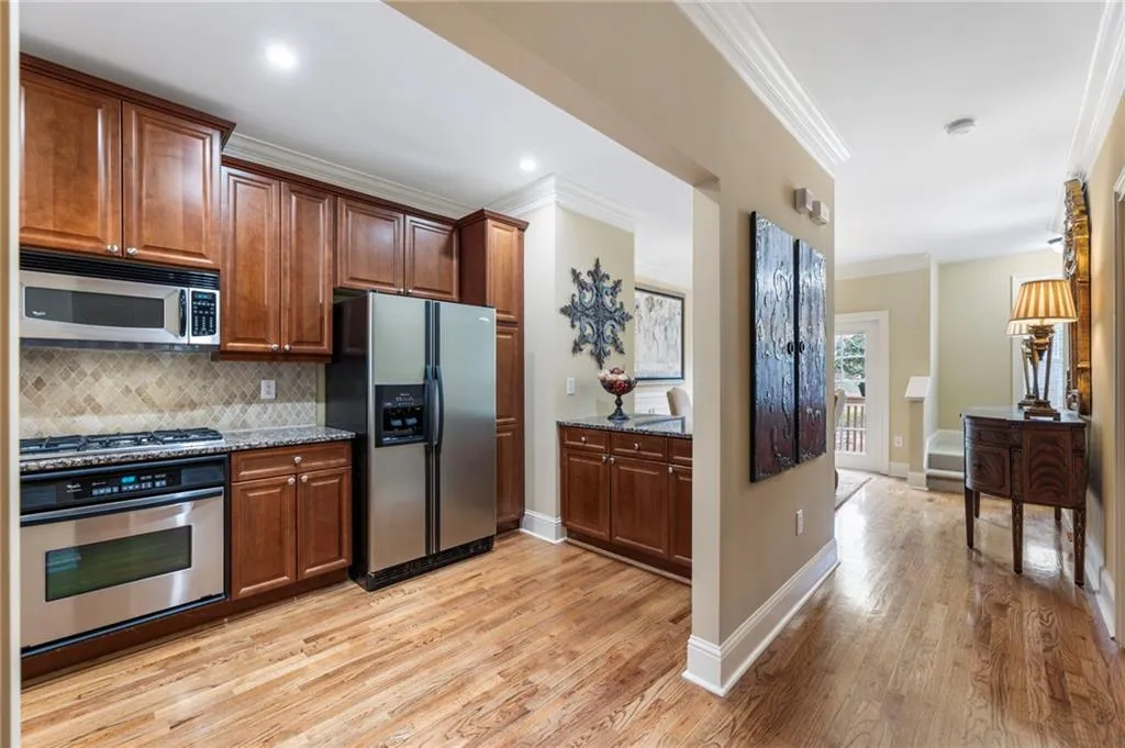Kitchen with stainless steel appliances, ornamental molding, light wood-style floors, decorative backsplash, and light stone countertops