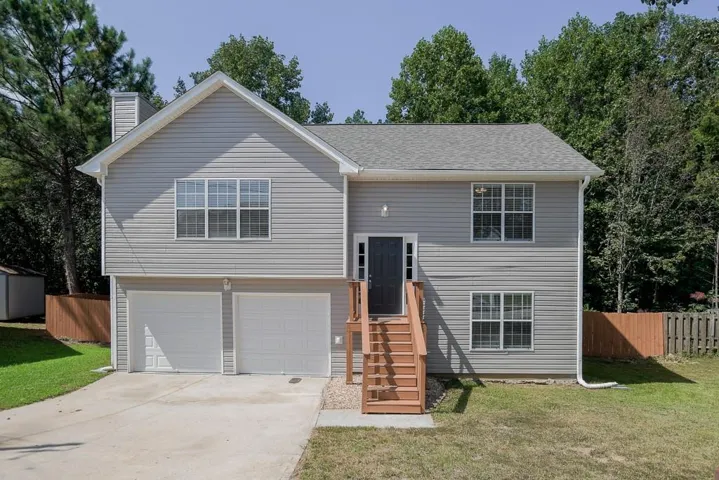 Gray siding exterior with white trim, two-car garage, dark entry door, and wood-finish stairs