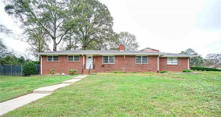 Brick exterior with white trim, front entry with white door and dark railings, concrete walkway, and a spacious front lawn