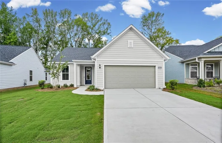 Light-toned siding exterior with an attached garage, paved driveway, and established landscaping