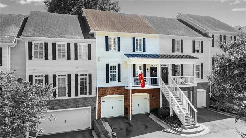 Two-story townhome with a brick and siding exterior, featuring two garage bays, a covered porch, and exterior shutters