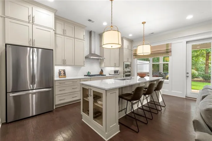 Kitchen featuring an expansive center island with seating, stainless steel appliances, white subway tile backsplash, and dark wood-finish flooring