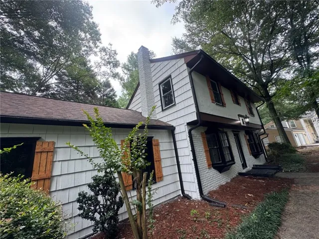 Two-story residence featuring white shingle and brick siding, a brown shingle roof, and a prominent white brick chimney