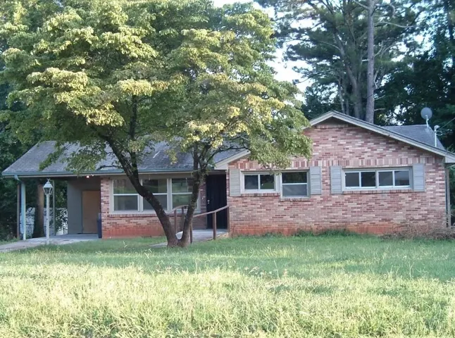 Brick exterior with gabled roofline, multiple windows, and a covered carport