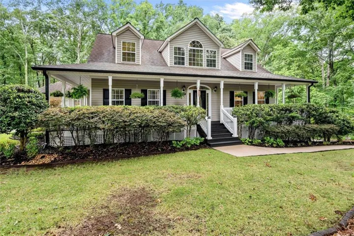Traditional-style residence featuring a wrap-around porch with white columns, light gray siding, and a dark shingle roof