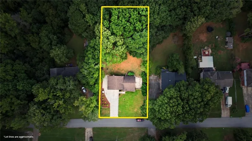 Expansive lot with mature tree coverage, a single-story residence, a paved driveway, and a partially cleared rear yard