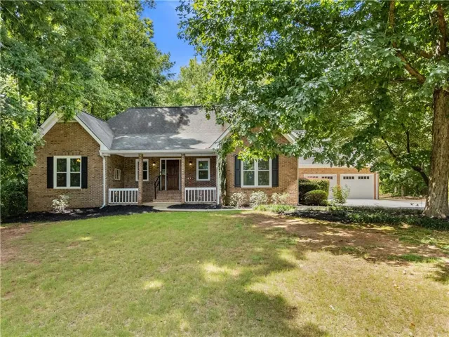 Charming brick ranch home featuring a welcoming front-facing covered porch with white railings, multiple windows with dark shutters, and a two-car attached garage