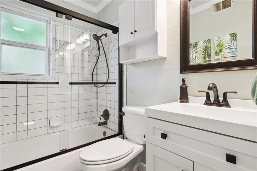 Full bathroom featuring vanity, crown molding, toilet, and shower / bath combination with glass door