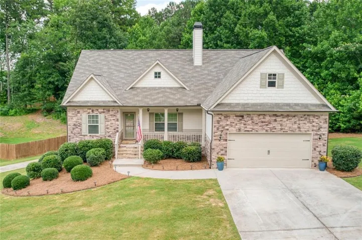 Gable-roof property featuring a stacked stone and shingle facade, a covered front porch, and an attached two-car garage