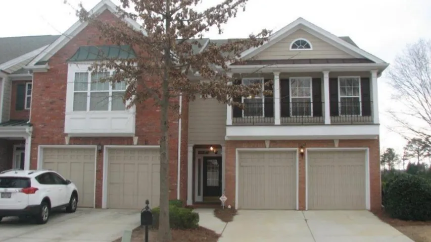 Brick and siding facade featuring a gabled roofline, multiple garage doors, and an upper-level porch with white columns