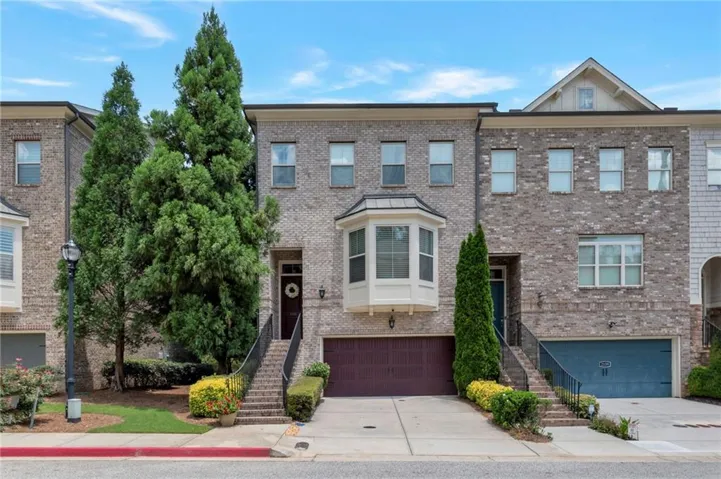 Brick exterior featuring multiple windows, a bay window on the second level, an attached two-car garage, and a concrete driveway