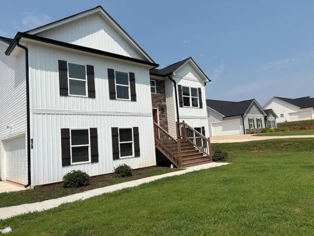 Two-story residence featuring white vertical siding, dark brown shutters, and a stone accent facade