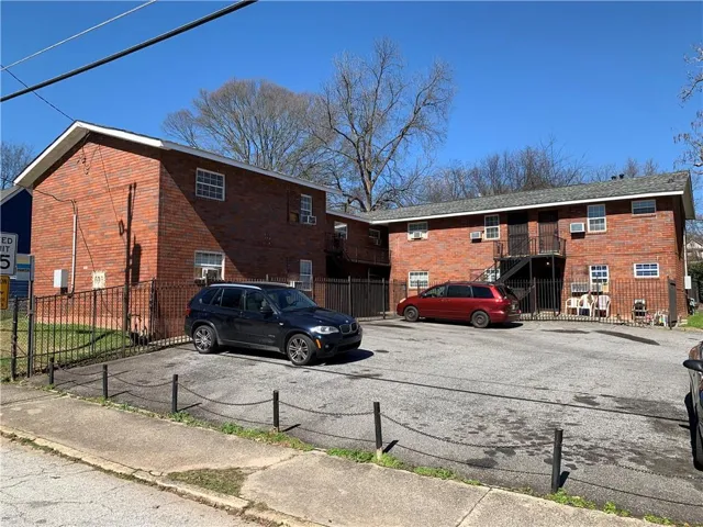 Brick exterior construction with multiple windows, black metal fencing, and a paved parking area