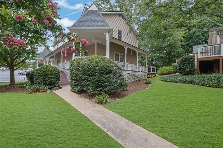 Two-story residence featuring a prominent turret with a shingled roof, extensive wrap-around porch with white railings, and siding exterior