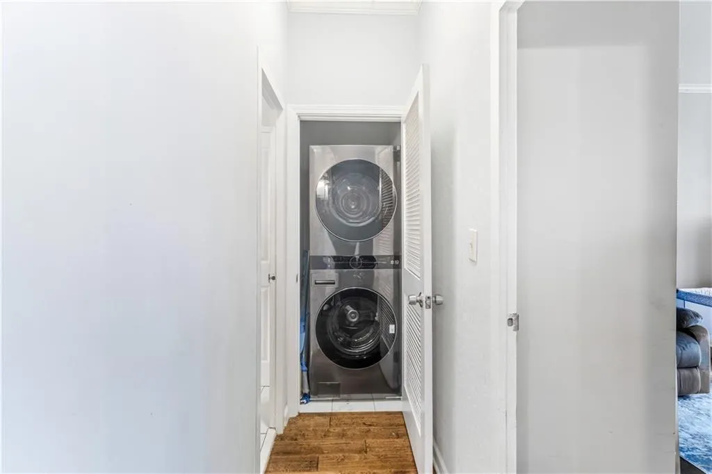 Laundry area with stacked washer and dryer, wood finished floors, and ornamental molding