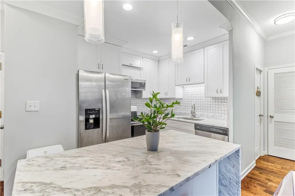 Kitchen with dark wood-style floors, stainless steel appliances, ornamental molding, white cabinets, and hanging light fixtures