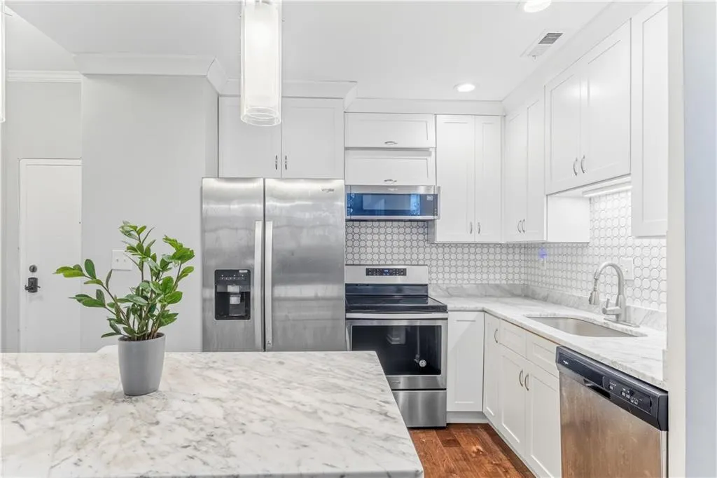 Kitchen with stainless steel appliances, white cabinets, light stone counters, and recessed lighting