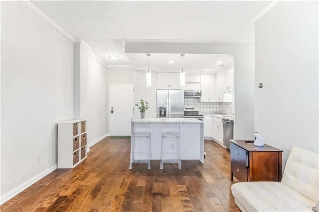 Kitchen with white cabinetry, stainless steel appliances, dark wood-type flooring, crown molding, and pendant lighting