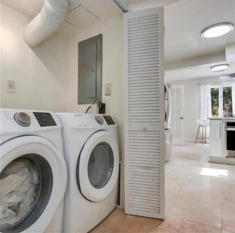 Laundry room with electric panel, independent washer and dryer, and light tile patterned flooring