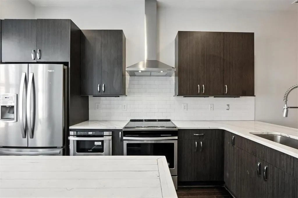 Kitchen featuring stainless steel appliances, wall chimney range hood, light stone countertops, and backsplash Kitchen featuring stainless steel appliances, wall chimney range hood, light stone countertops, and backsplash