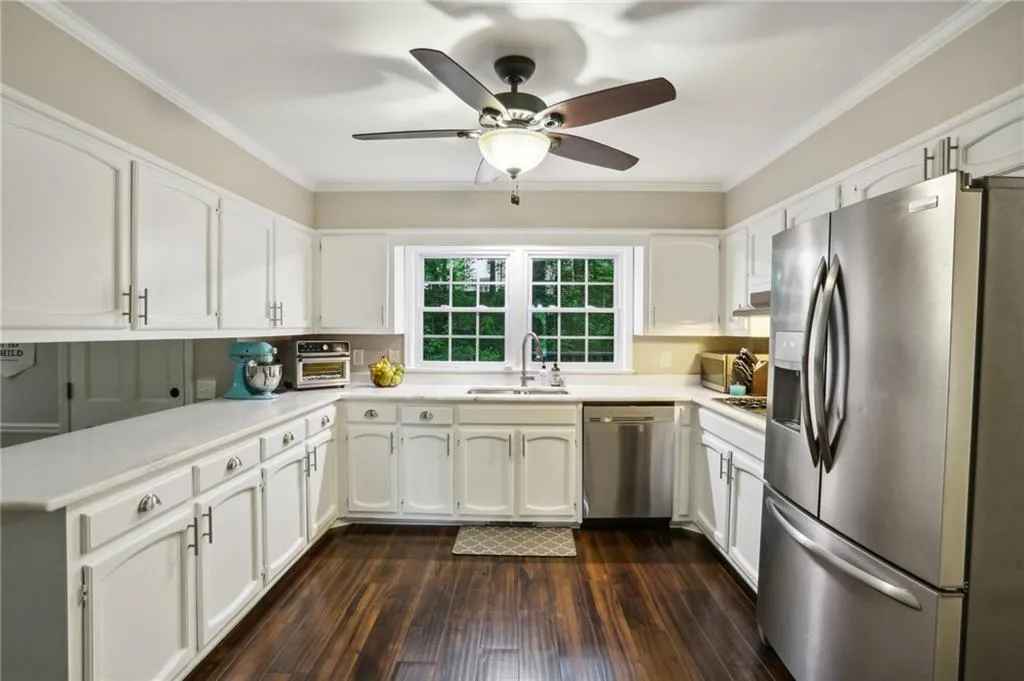 Kitchen featuring dark wood-type flooring, appliances with stainless steel finishes, white cabinets, sink, and ceiling fan