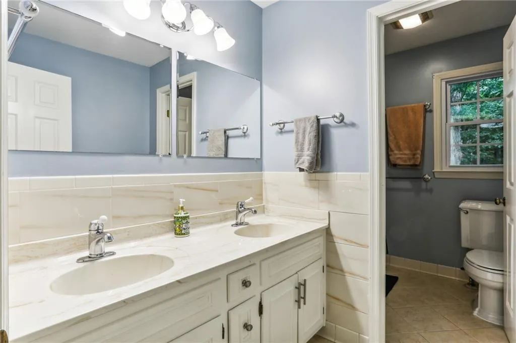 Bathroom featuring tile flooring, double sink vanity, tile walls, and toilet