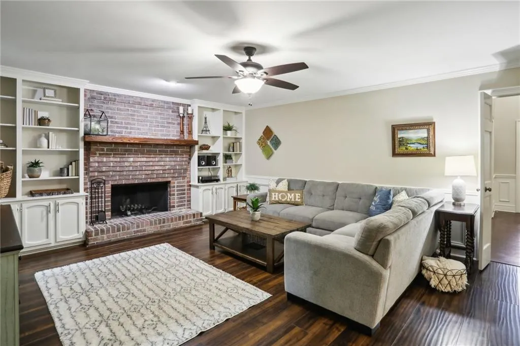 Living room featuring brick wall, ornamental molding, a fireplace, dark hardwood / wood-style floors, and ceiling fan