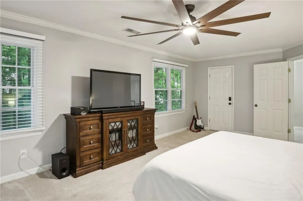 Carpeted bedroom featuring crown molding, multiple windows, and ceiling fan