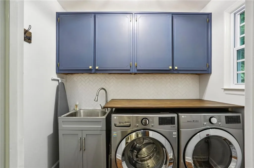 Clothes washing area with sink, washer and clothes dryer, and cabinets