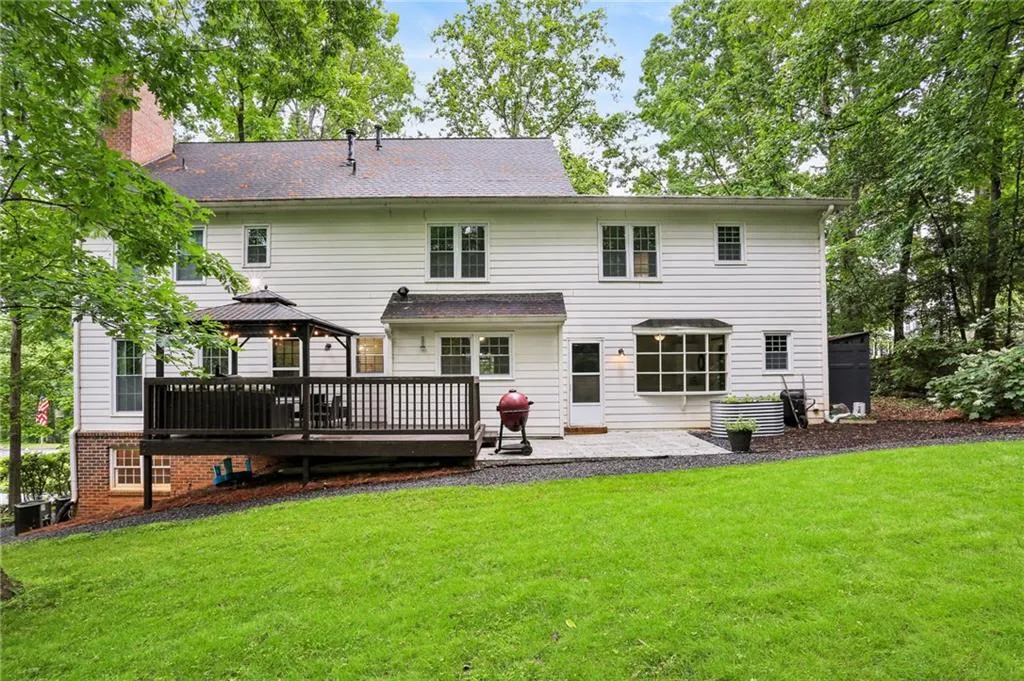 Rear view of house with a wooden deck, a gazebo, central AC unit, and a lawn