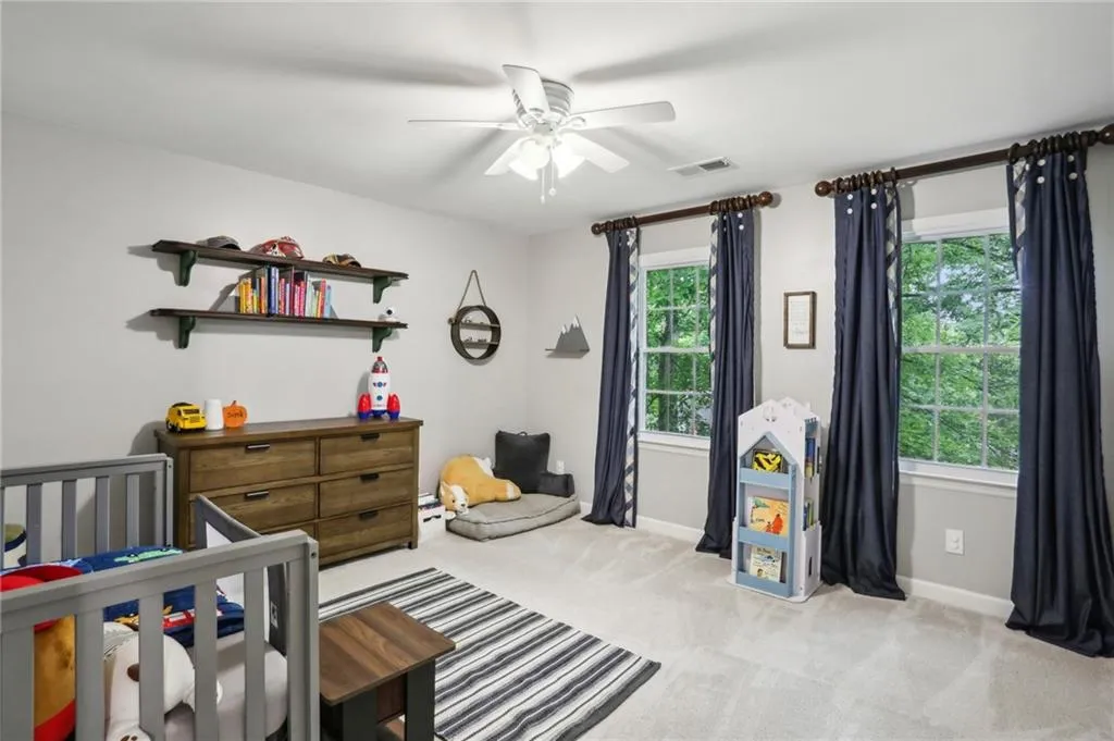 Bedroom featuring ceiling fan, light colored carpet, and a nursery area