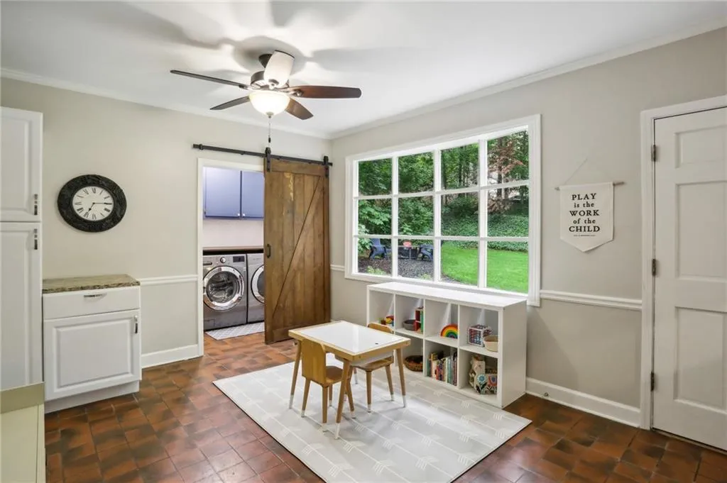 Dining space featuring separate washer and dryer, crown molding, a barn door, dark tile flooring, and ceiling fan