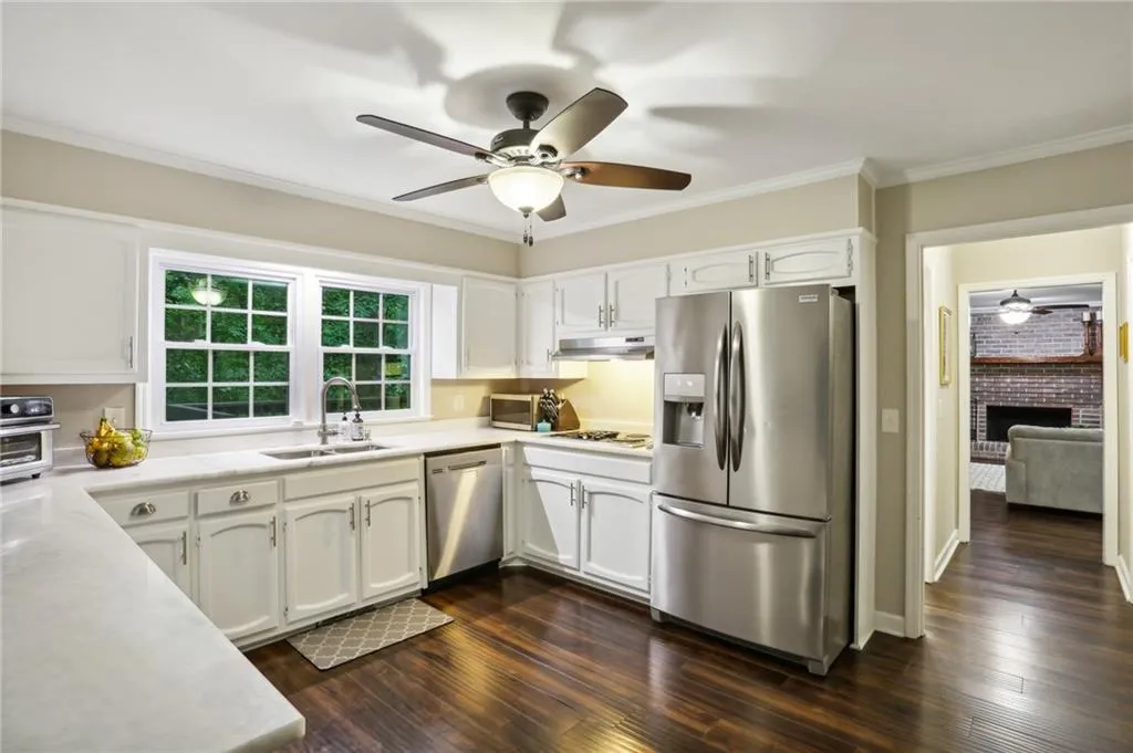 Kitchen featuring stainless steel appliances, dark hardwood / wood-style floors, a brick fireplace, sink, and ceiling fan