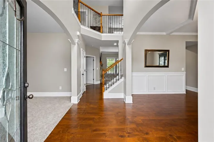 Two-story foyer with a leaded glass entry door, wood-finish flooring, wainscoting, and a prominent staircase with wood handrails and iron balusters