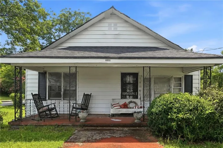White siding exterior featuring a covered front porch with dark metal support columns, a dark shingled roof, and a visible address number