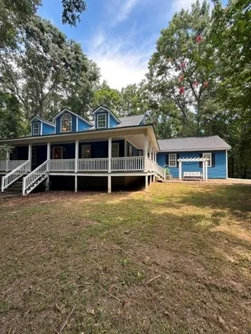 Blue exterior with white trim, a sweeping covered porch, multiple dormer windows, and a white pergola feature