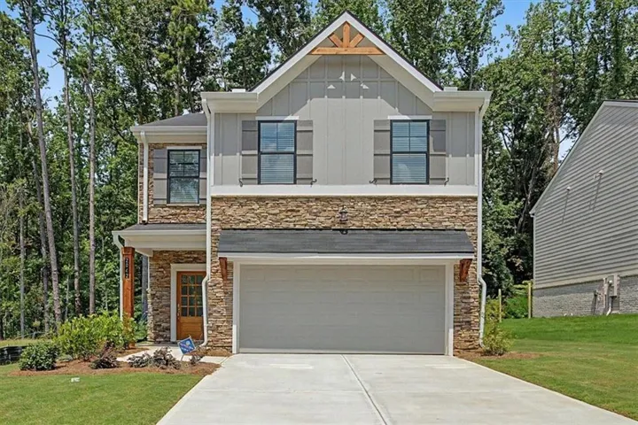 Crafted exterior featuring stacked stone accents, vertical panel siding, decorative gable truss, attached two-car garage, and a paneled front door
