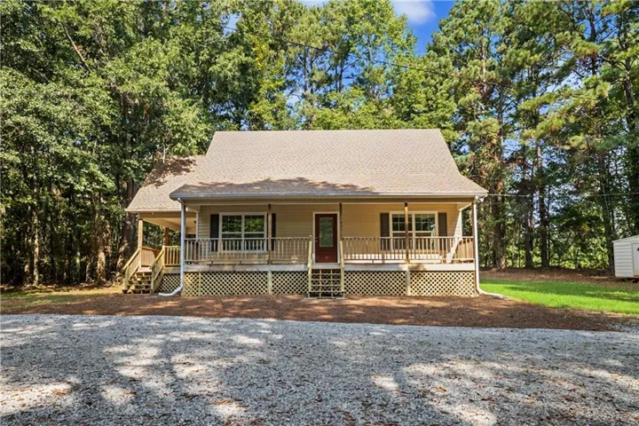 Two-story residence featuring a covered front porch with wood railings and lattice skirting, a gravel driveway, and surrounding mature trees
