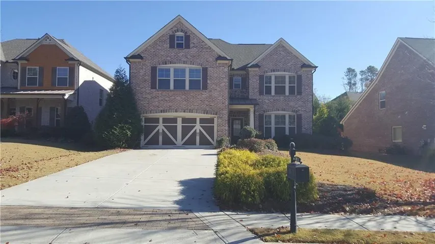 Traditional two-story brick exterior featuring a two-car garage with decorative doors, a concrete driveway, and mature landscaping