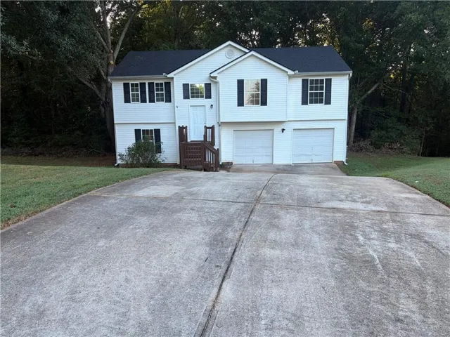 Split-level residence featuring white siding, a dark roof, a two-car garage, and a concrete driveway